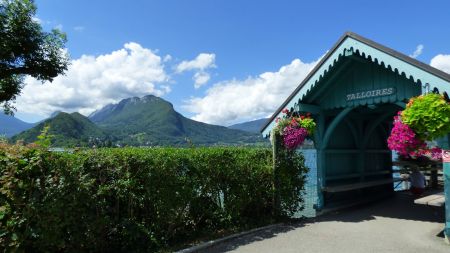 On se dirige vers le bout de la jetée (juste après ce bel abri fleuri). Par-dessus la haie, on voit déjà la presqu’île de Duingt, entre les extrémités de la crête du Taillefer et de la Montagne d’Entrevernes.